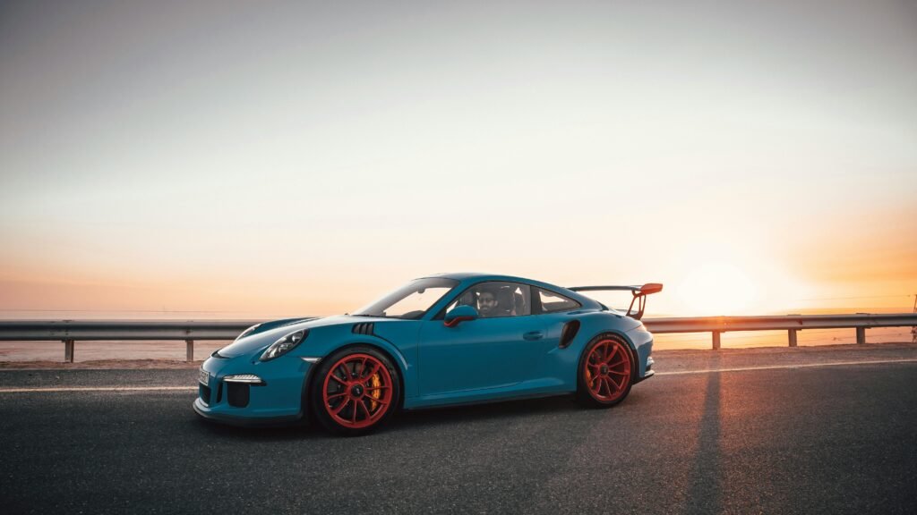 A sleek blue sport car on an open highway against a stunning sunset backdrop.